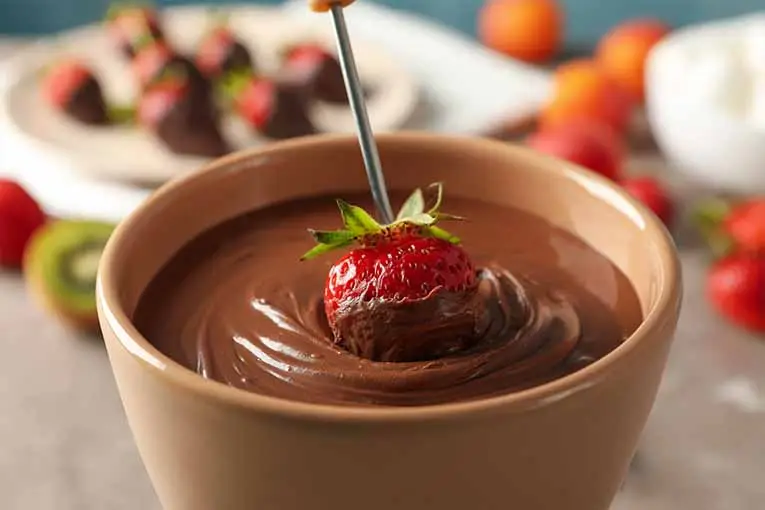 a strawberry being dipped in chocolate
